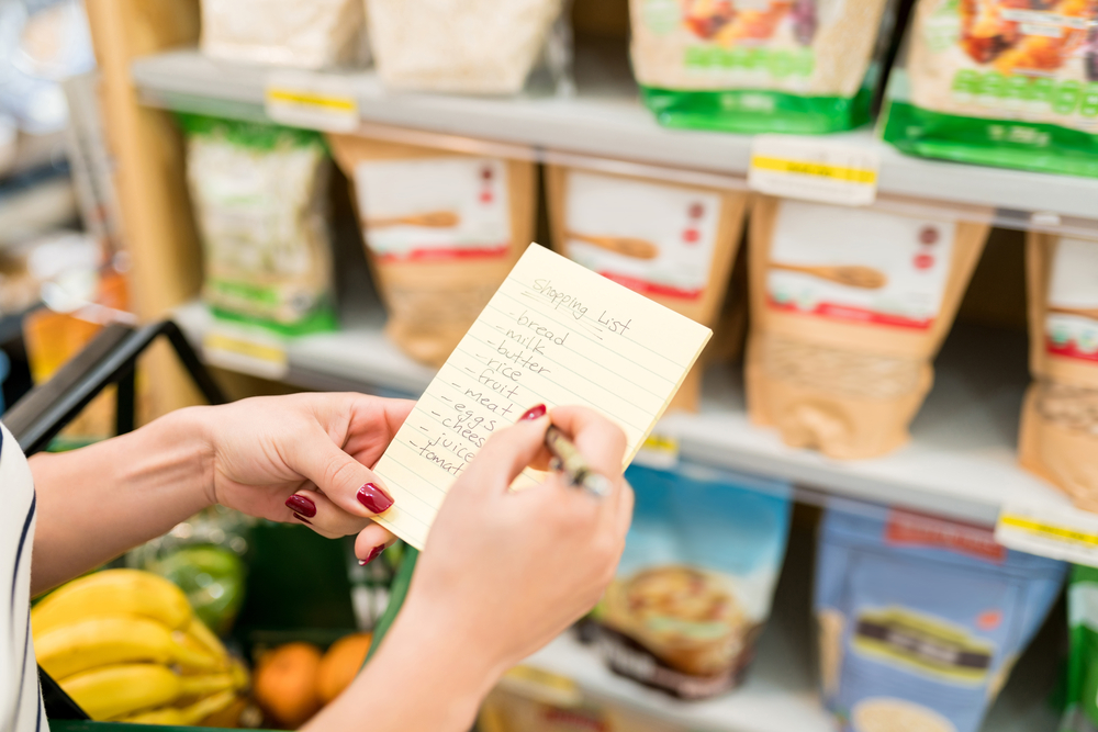 A woman's hands holding a grocery shopping list and a pen