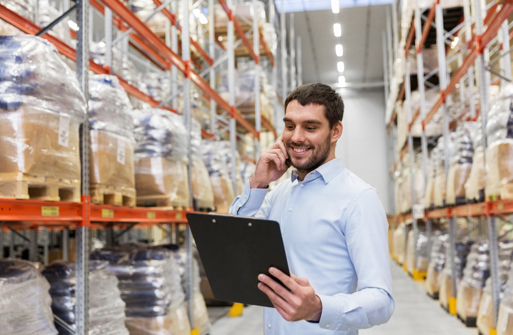 A man in a warehouse holding a file and a phone