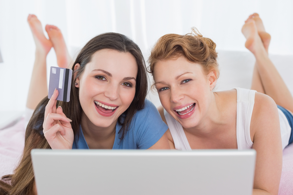 Two women in bed with laptop and credit card
