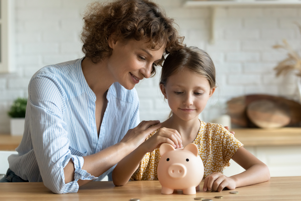 A woman and a girl putting money in a piggy bank