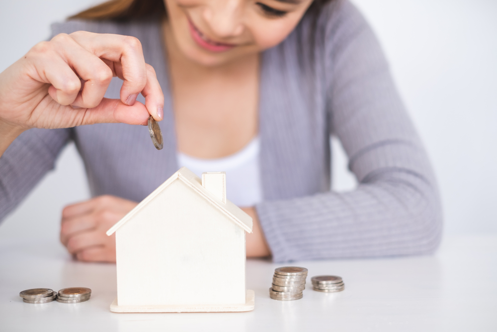 A woman putting coins in a house-shaped money box