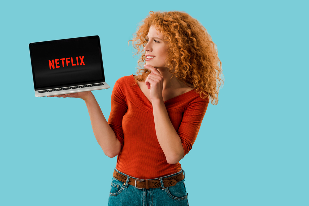 A woman holding a laptop with Netflix flashed on screen
