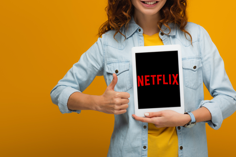 A woman holding a tablet with Netflix flashed on screen