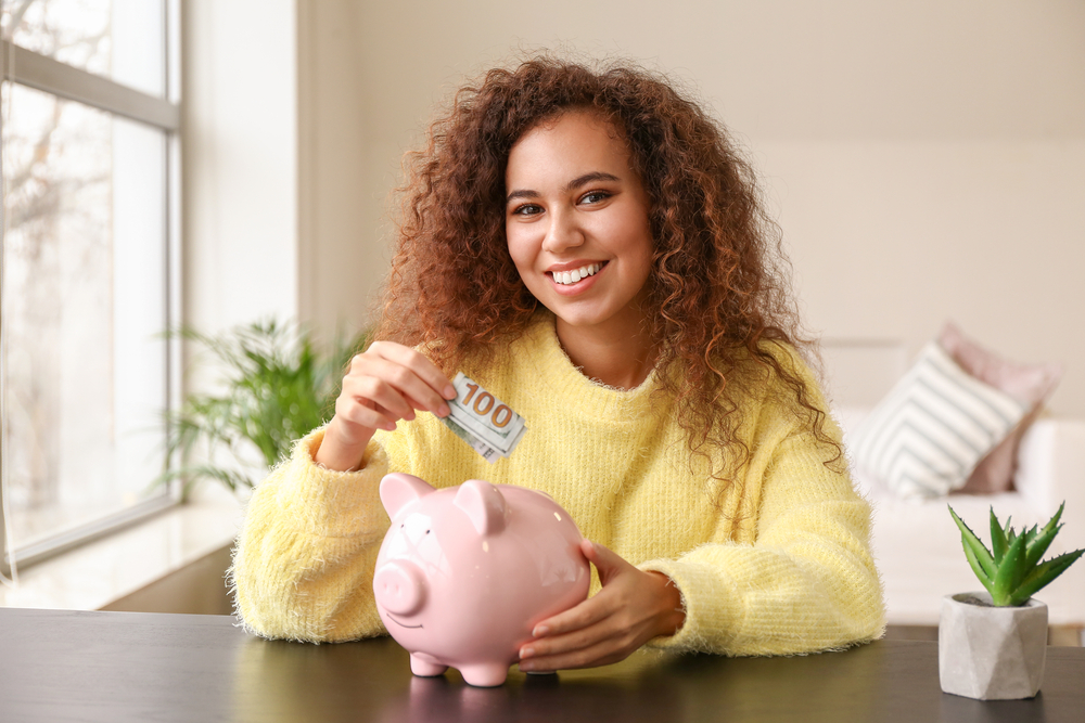 A woman putting a bill in a piggy bank