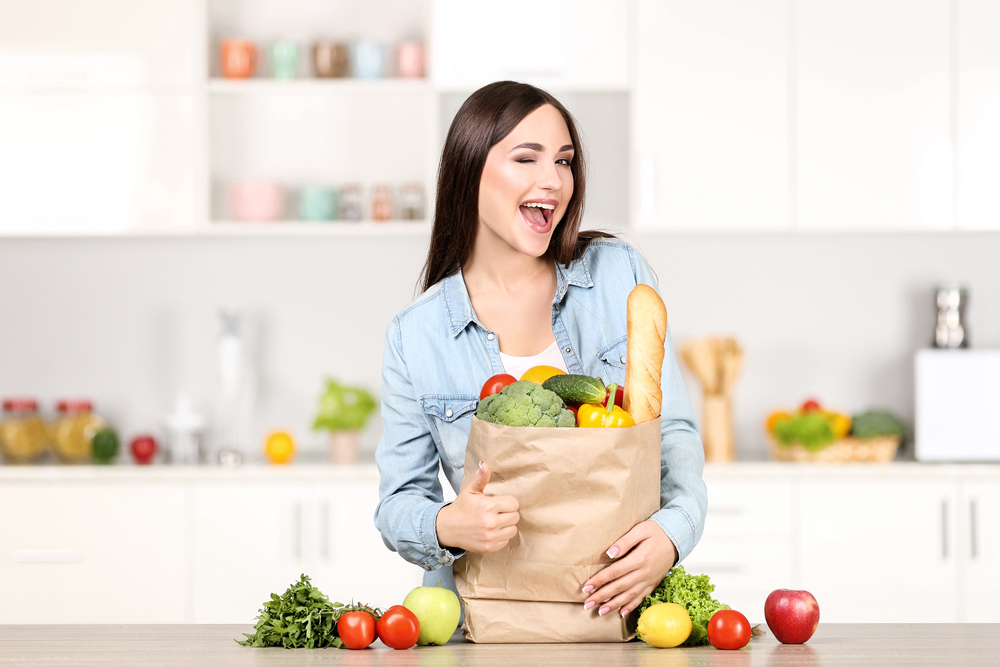A woman with grocery items in the kitchen