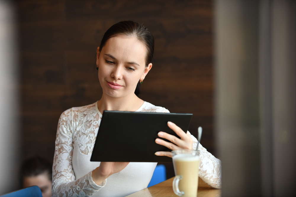 A woman looking at a tablet over coffee