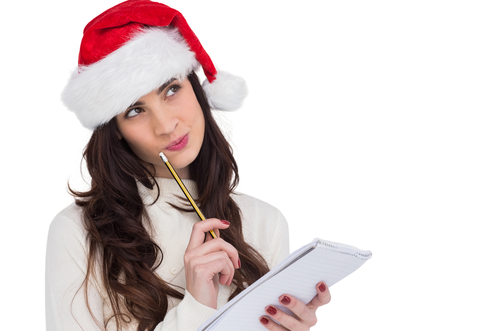 A woman wearing a Santa hat, holds a pen and paper