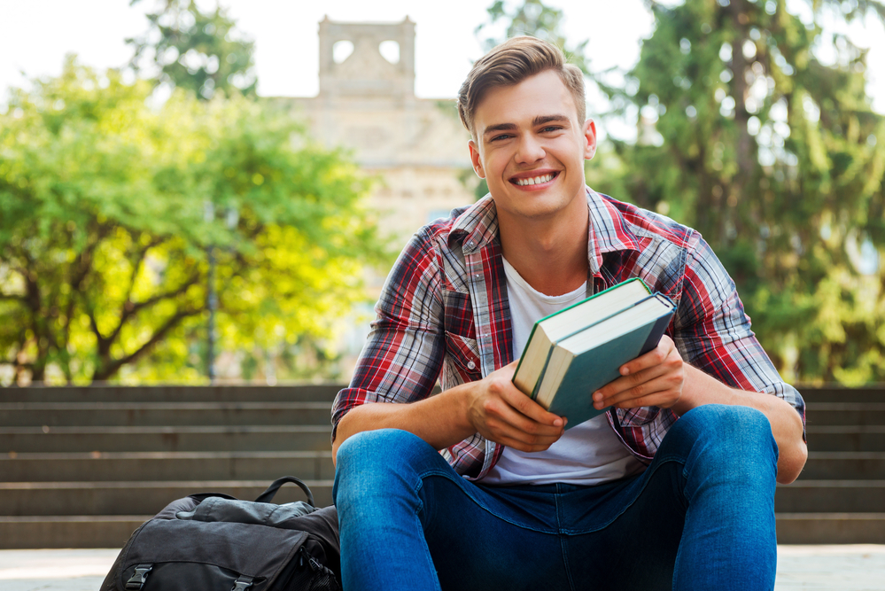 A young man sitting on the campus steps holding books
