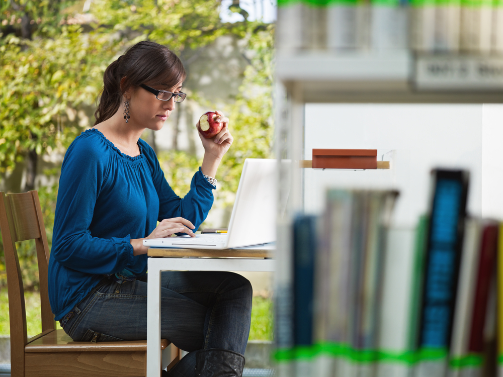 A young woman holding an apple and reading